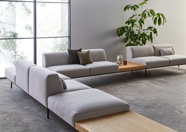 A grey corner sofa can be seen with tables and a plant. Cushions are on the sofa. The location is a waiting area.